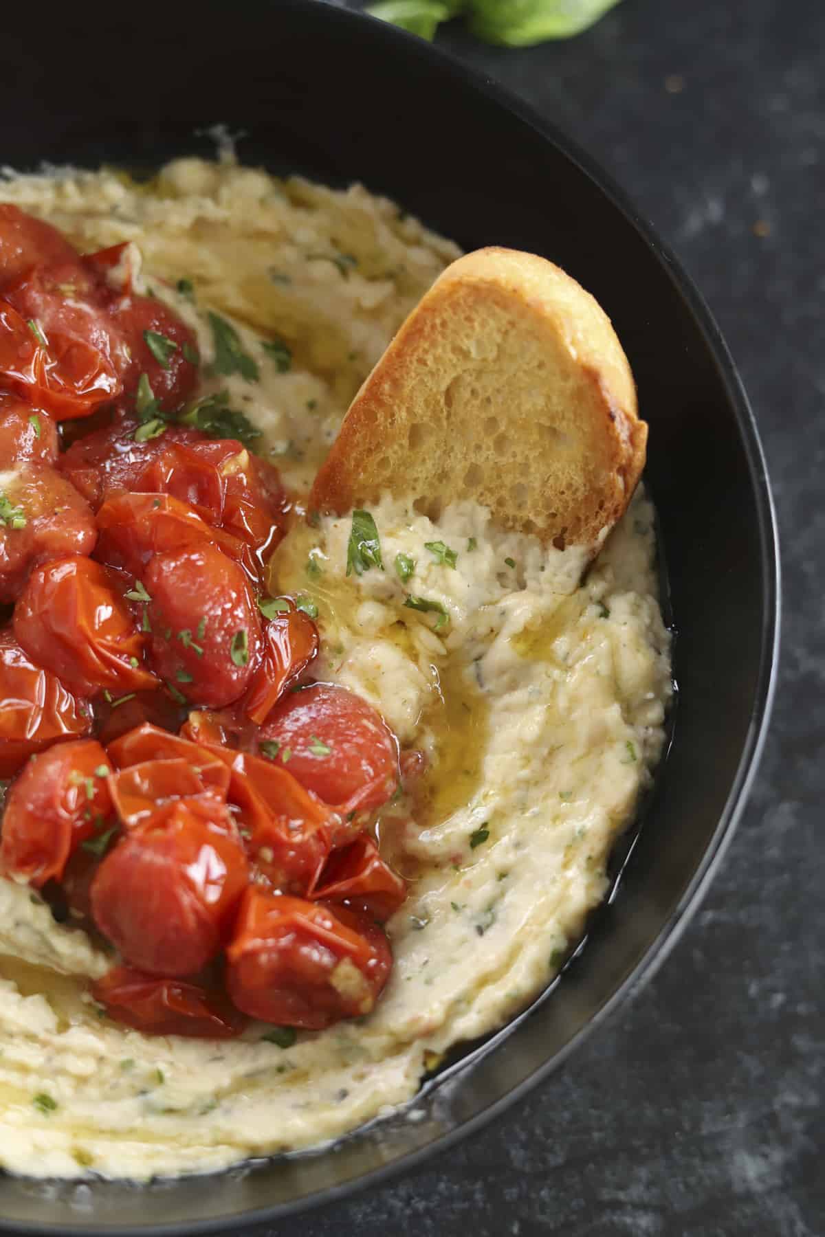 bowl of white bean dip with roasted tomatoes and baguette.