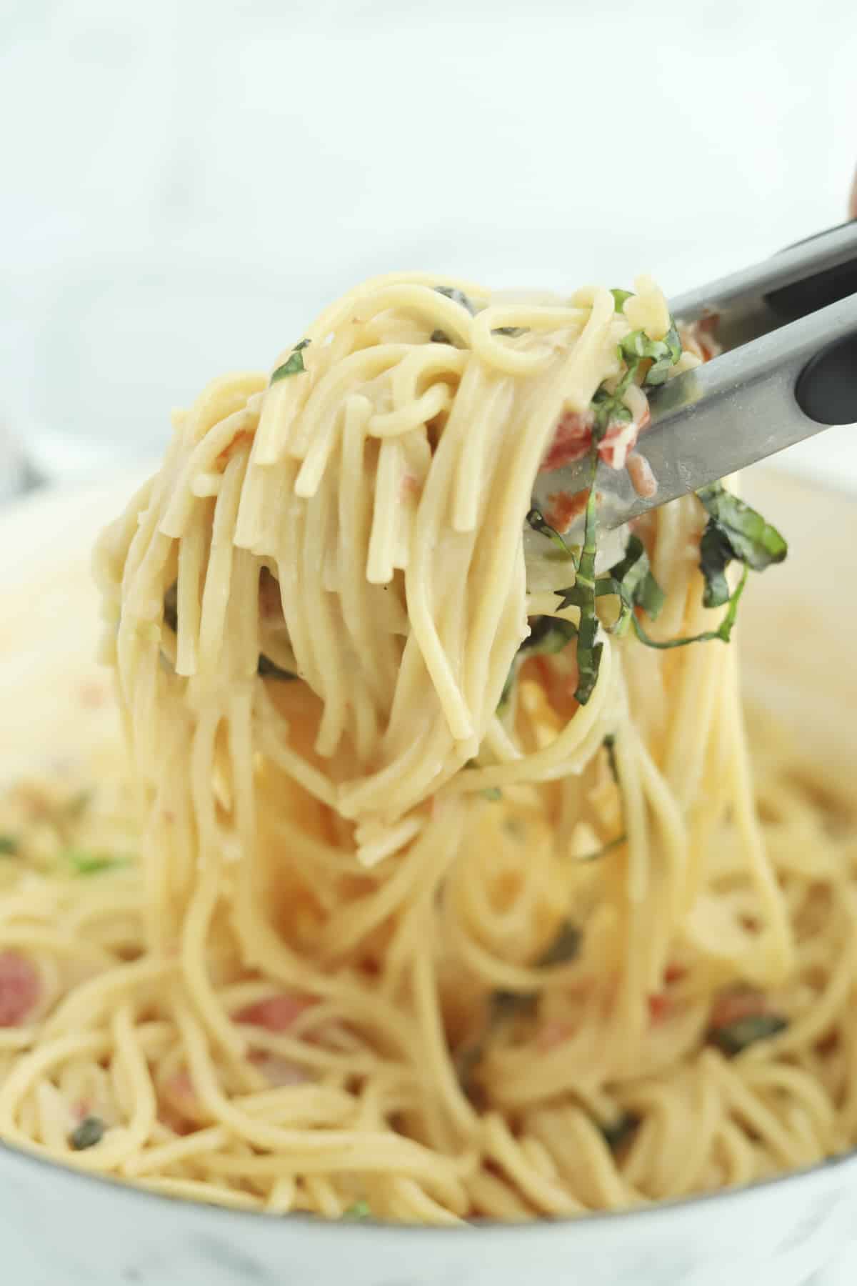 tongs lifting a portion of Parmesan pasta from a pot