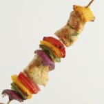 a hand holding an oven-baked chipotle chicken skewer with red, yellow, and green peppers and red onion