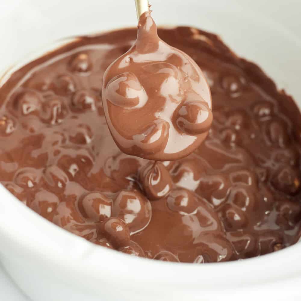 melted chocolate, hazelnut butter, and hazelnuts being spooned out of a crock pot to from crock pot candy