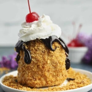 fried ice cream on a plate topped with chocolate sauce, whipped cream, and a cherry