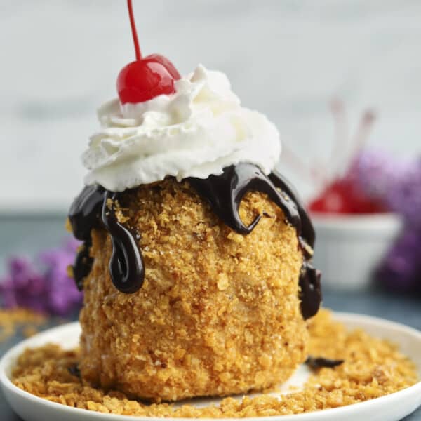 fried ice cream on a plate topped with chocolate sauce, whipped cream, and a cherry.