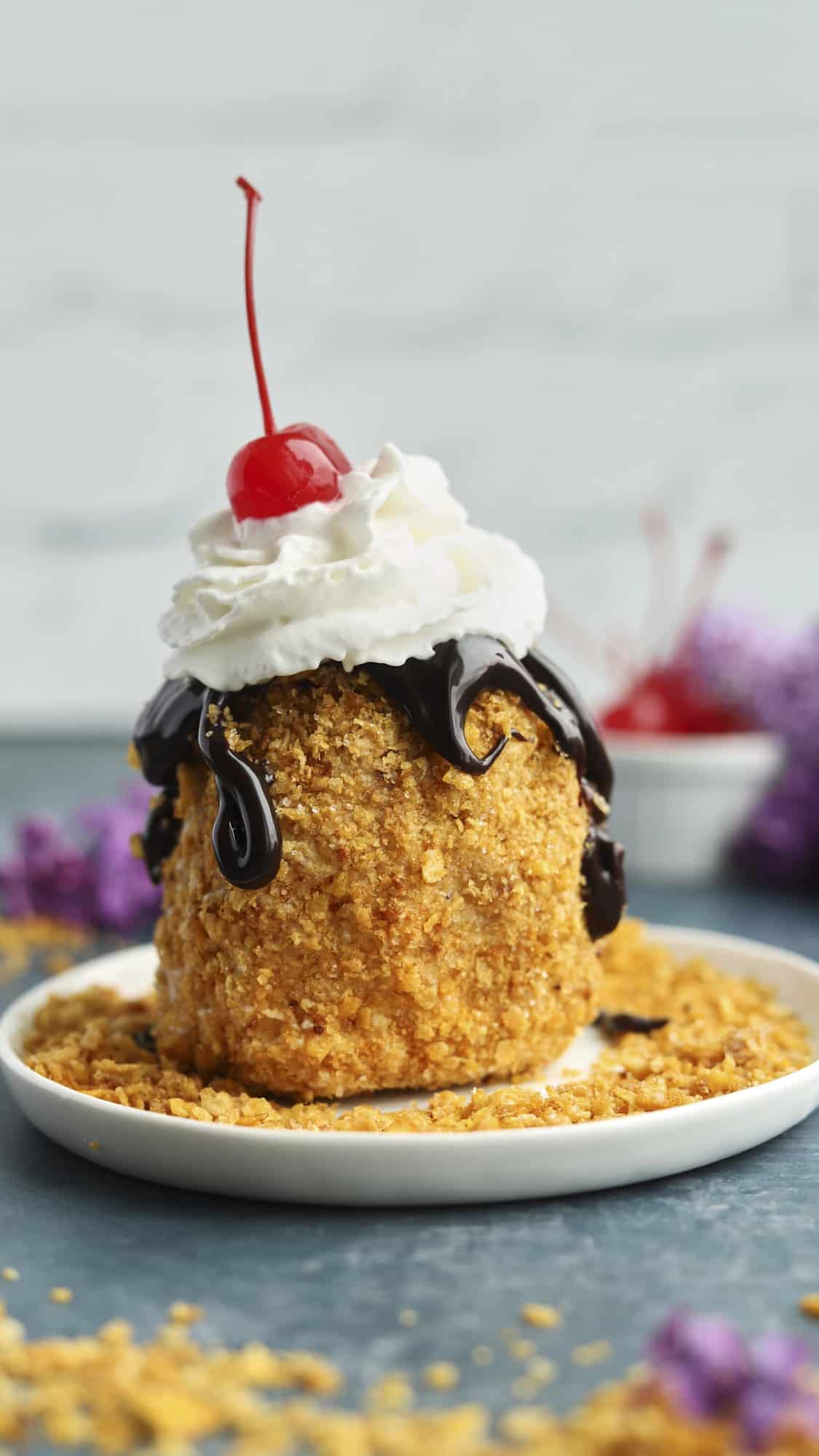 fried ice cream on a plate topped with chocolate sauce, whipped cream, and a cherry.