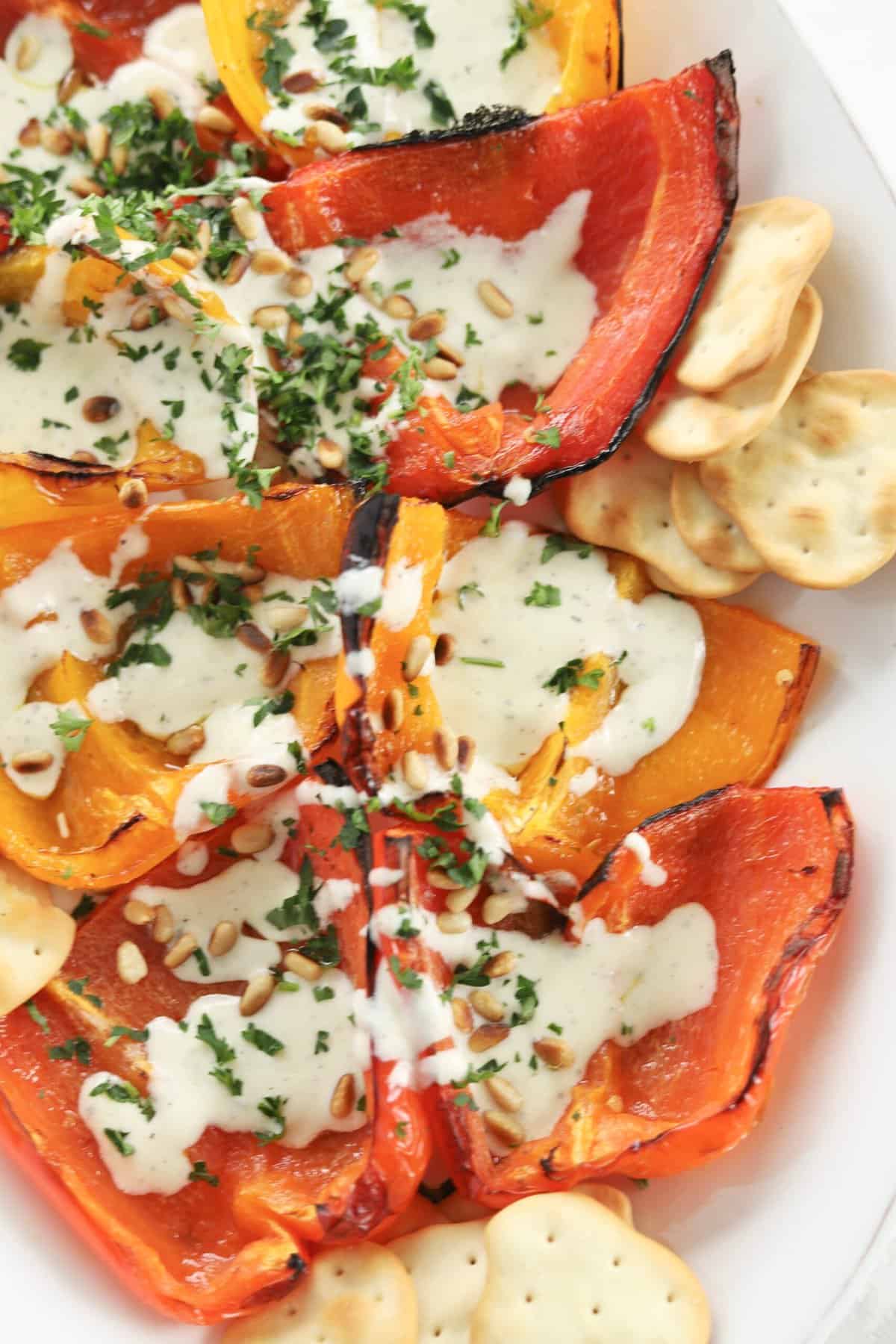 close up image of roasted peppers topped with whipped feta recipe, pine nuts, and parsley with crackers on the side