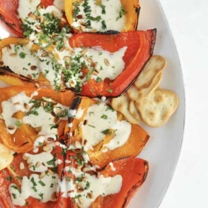 close up image of roasted peppers topped with whipped feta recipe, pine nuts, and parsley with crackers on the side