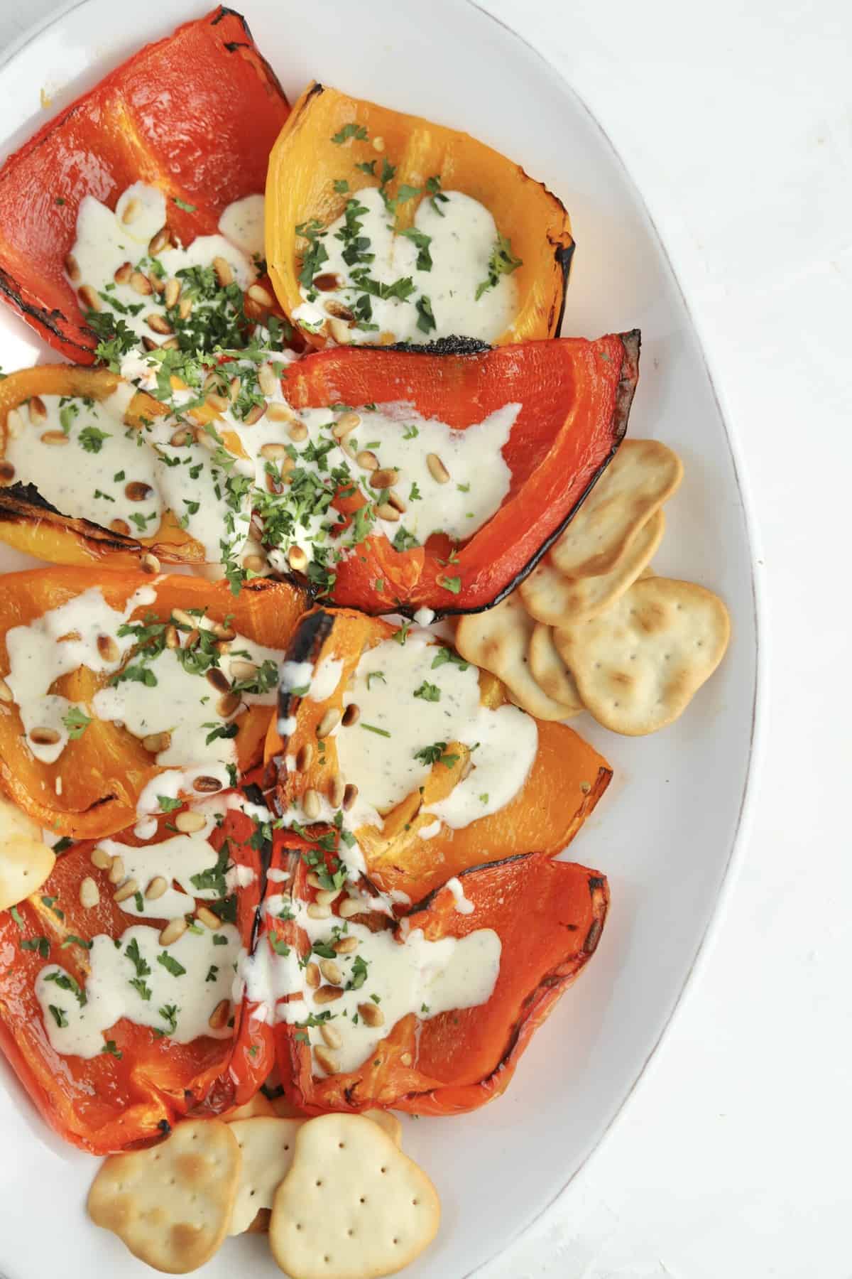 close up image of roasted peppers topped with whipped feta recipe, pine nuts, and parsley with crackers on the side