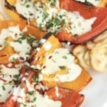 a white serving dish full of quartered roasted peppers and crackers topped with whipped feta, pine nuts, and chopped parsley
