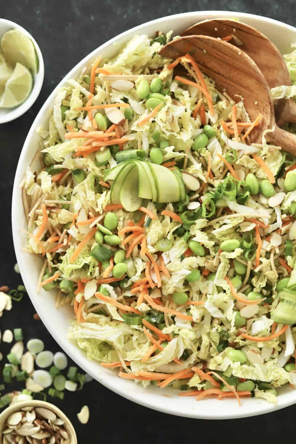 overhead image of a white bowl full of tossed cucumber thai salad with wooden salad spoons in the bowl on the side