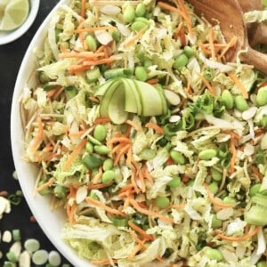 overhead image of a white bowl full of tossed cucumber thai salad with wooden salad spoons in the bowl on the side