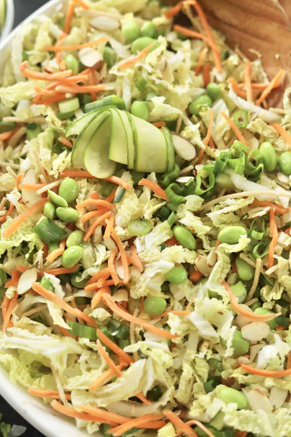 close up image of a tossed cucumber thai salad recipe made with edamame, carrots, cucumber, slivered almonds, green onions, and cilantro in a white bowl