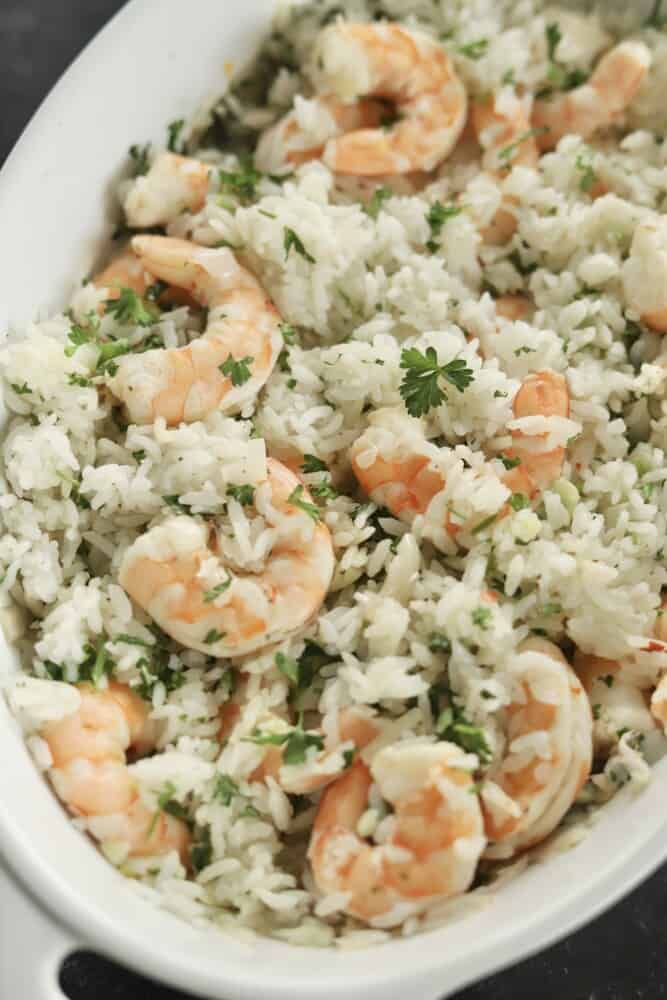 a white baking dish with lemon garlic shrimp and rice topped with fresh parsley.