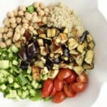 overhead image of quinoa, chickpeas, roasted eggplant, cucumber, and tomatoes in a bowl ready to be combined for roasted eggplant salad