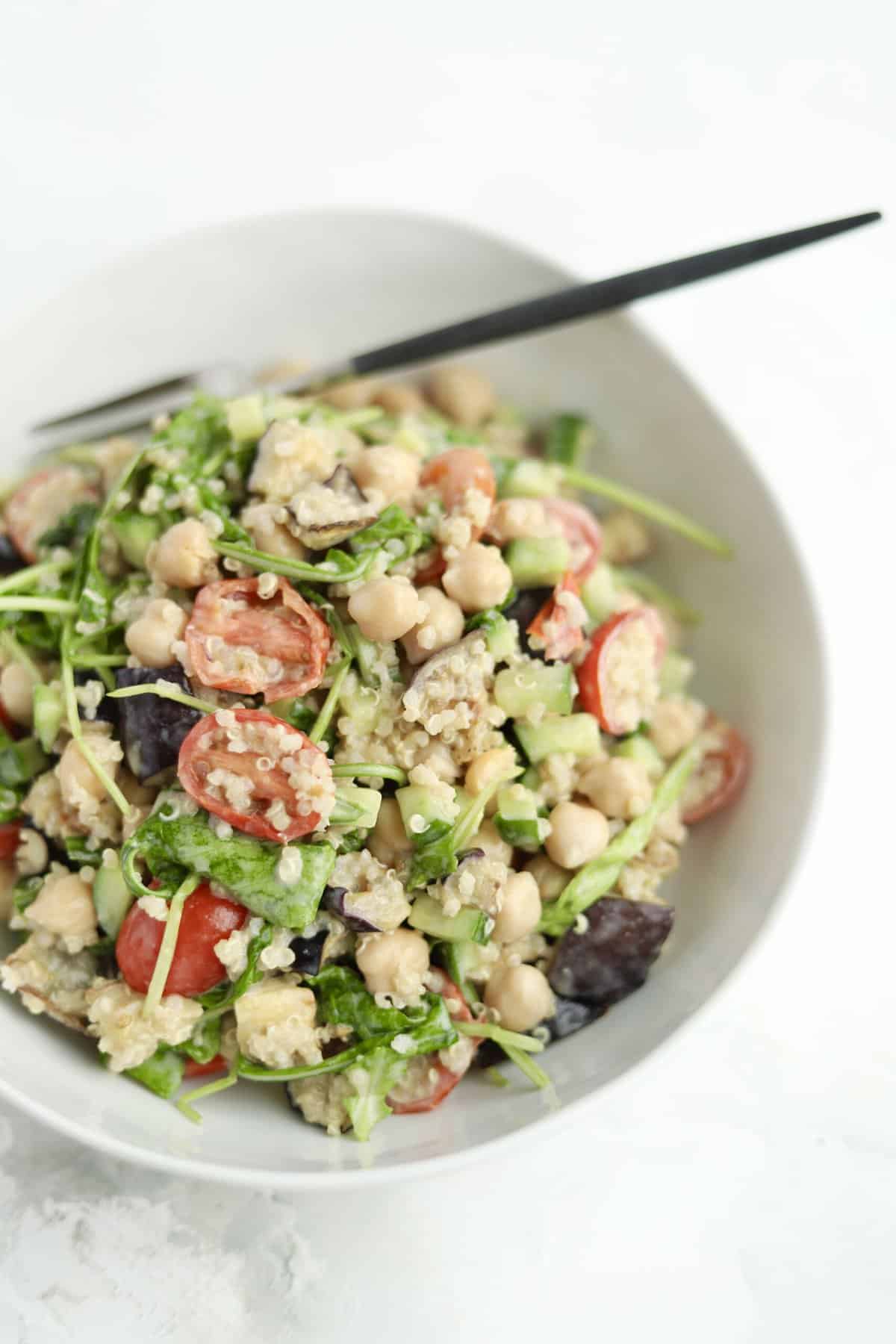 vegan roasted eggplant salad in a white bowl with tahini dressing and quinoa and a chopstick sticking out