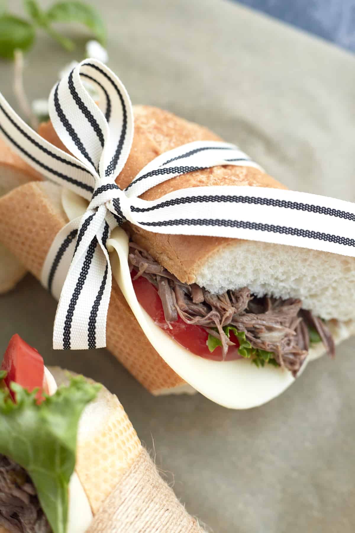 one po' boy sandwich wrapped in ribbon with lettuce, tomatoes, and cheese