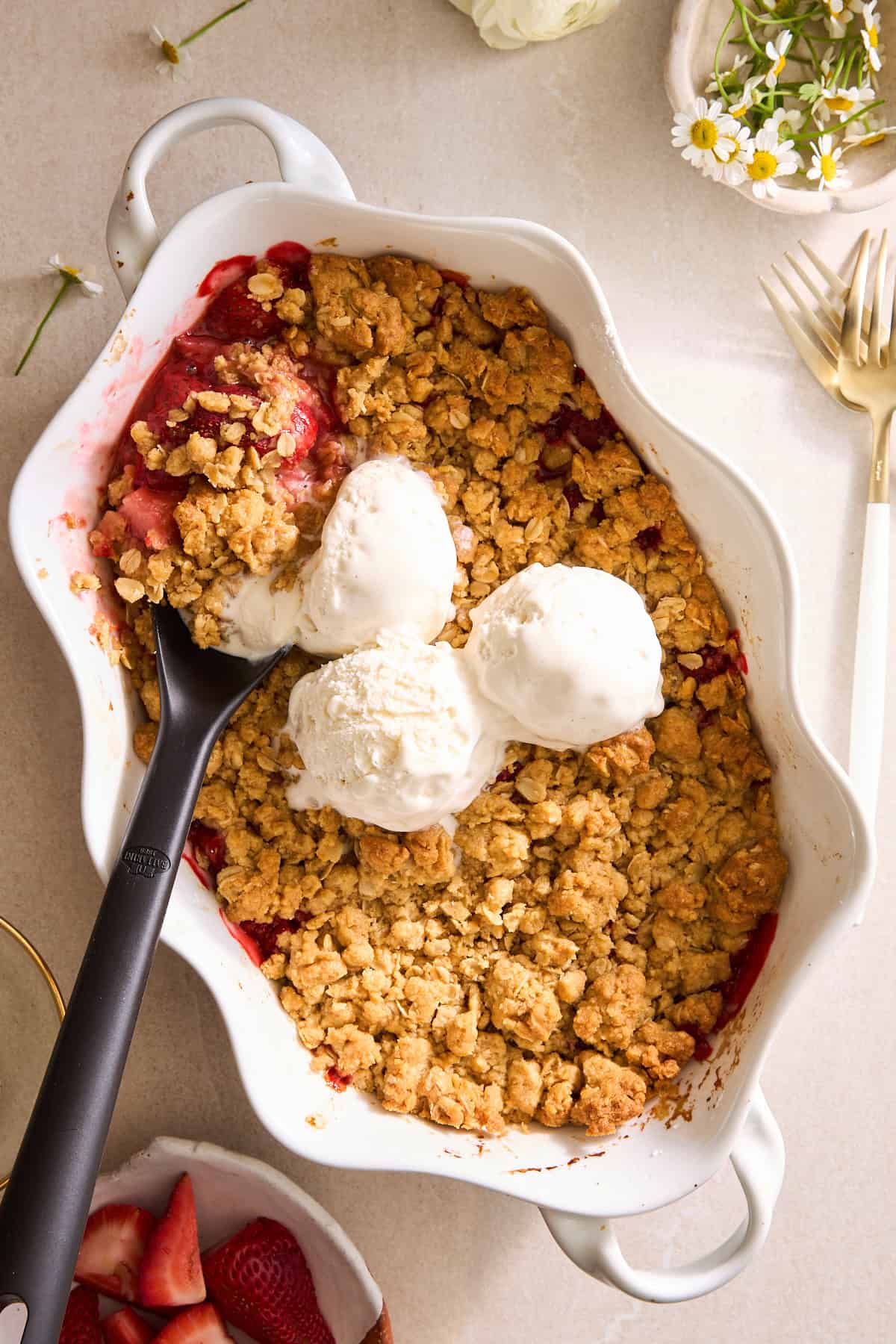 A dish of strawberry crisp topped with three scoops of vanilla ice cream with a spoon digging in. 