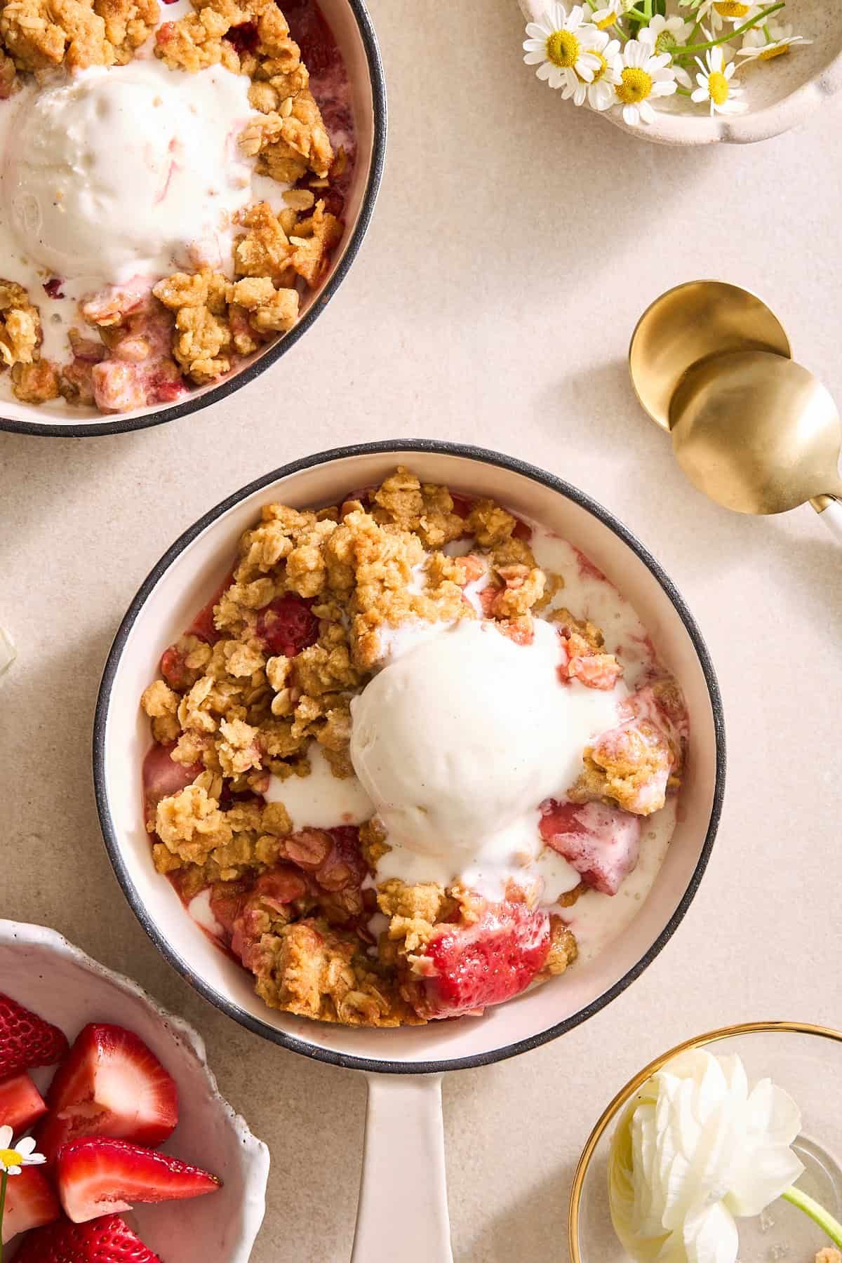 Two bowls of strawberry crisp topped with vanilla ice cream.