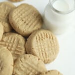 a pile of baked easy peanut butter cookies with a glass jar of milk on the side
