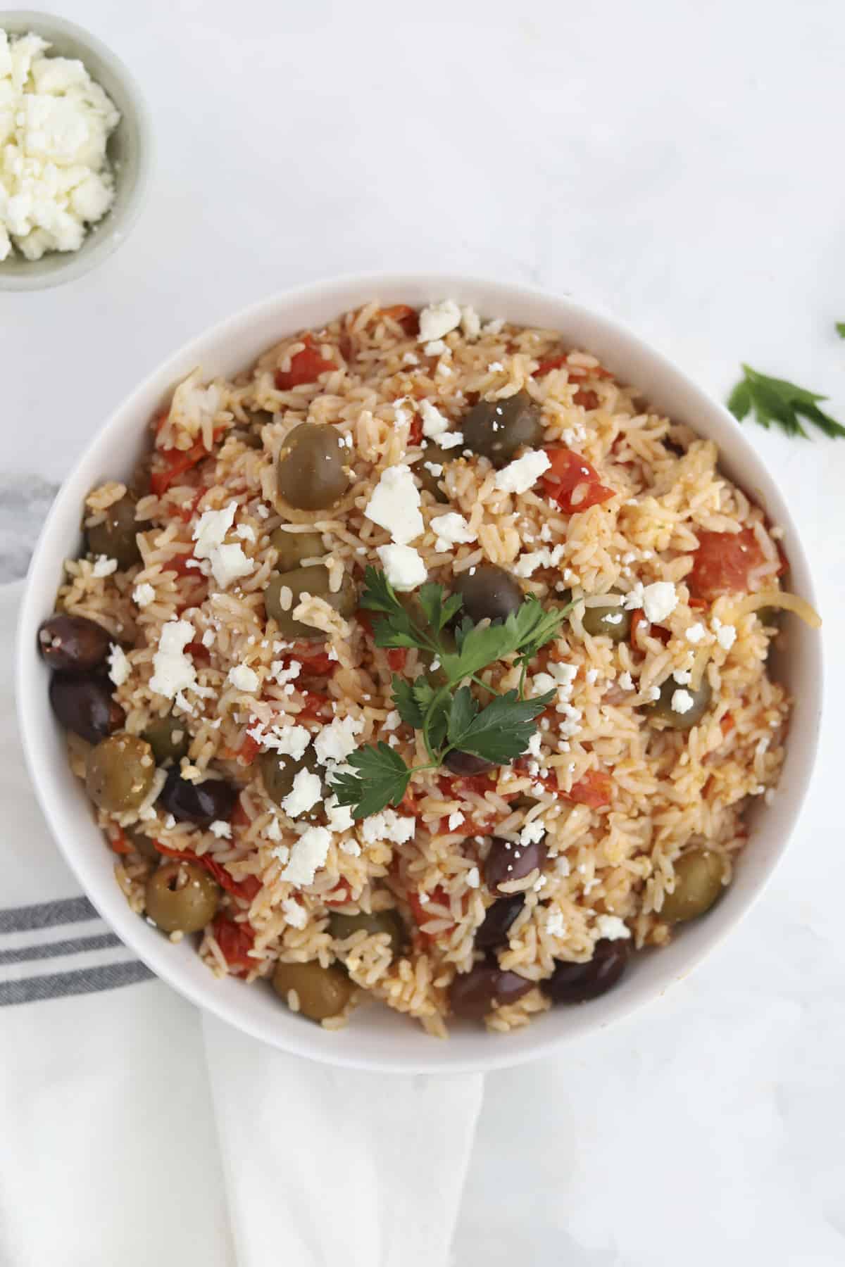 greek rice in a bowl topped with feta and fresh herbs