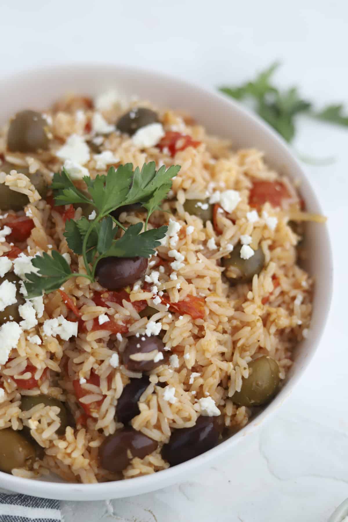 closeup image of a bowl of Greek rice bake topped with feta and fresh herbs