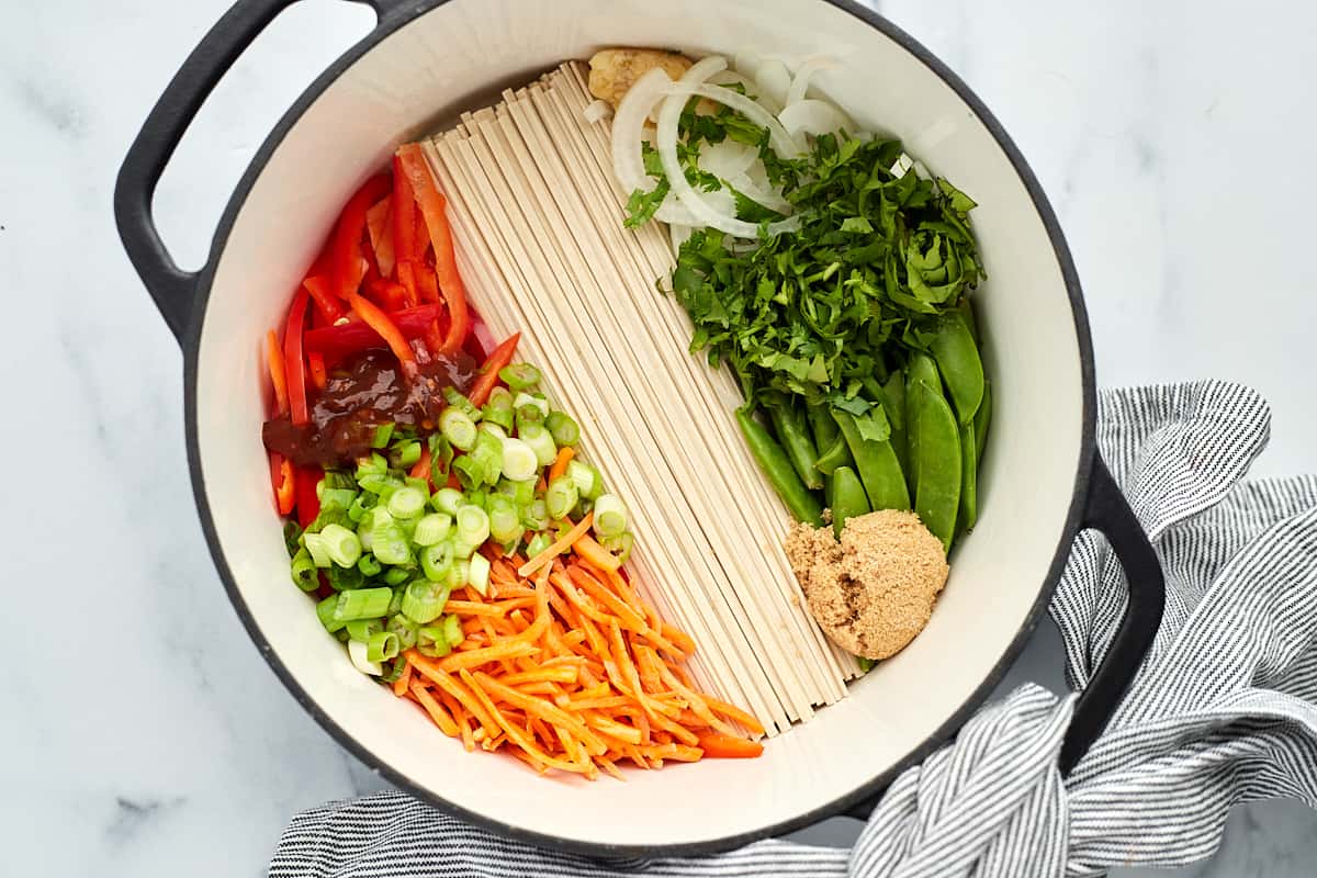 a pot full of veggies and rice noodles for ramen. 