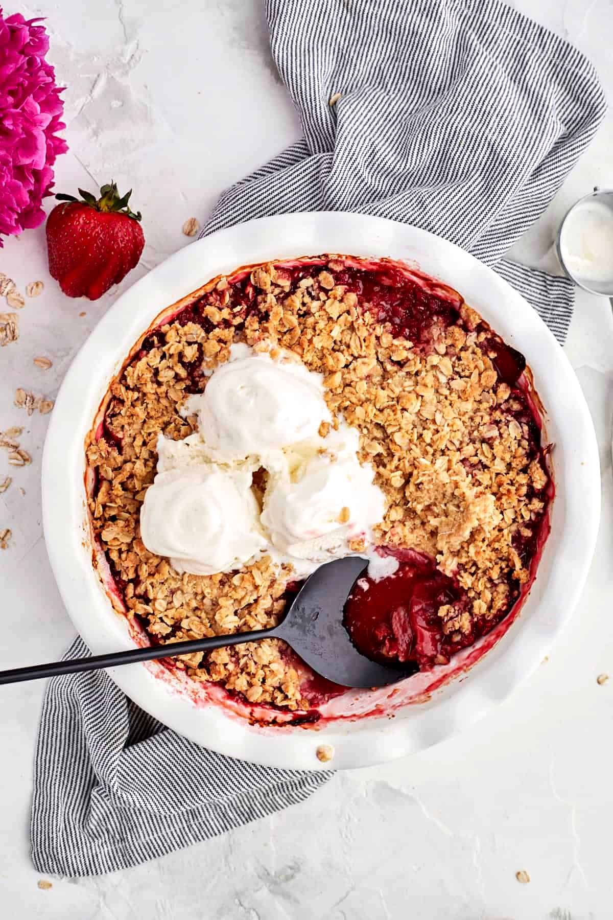 Strawberries in pie dish with oat crumble, ice cream and serving spoon