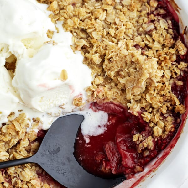 a spoon dipping into strawberry cobbler topped with vanilla ice cream