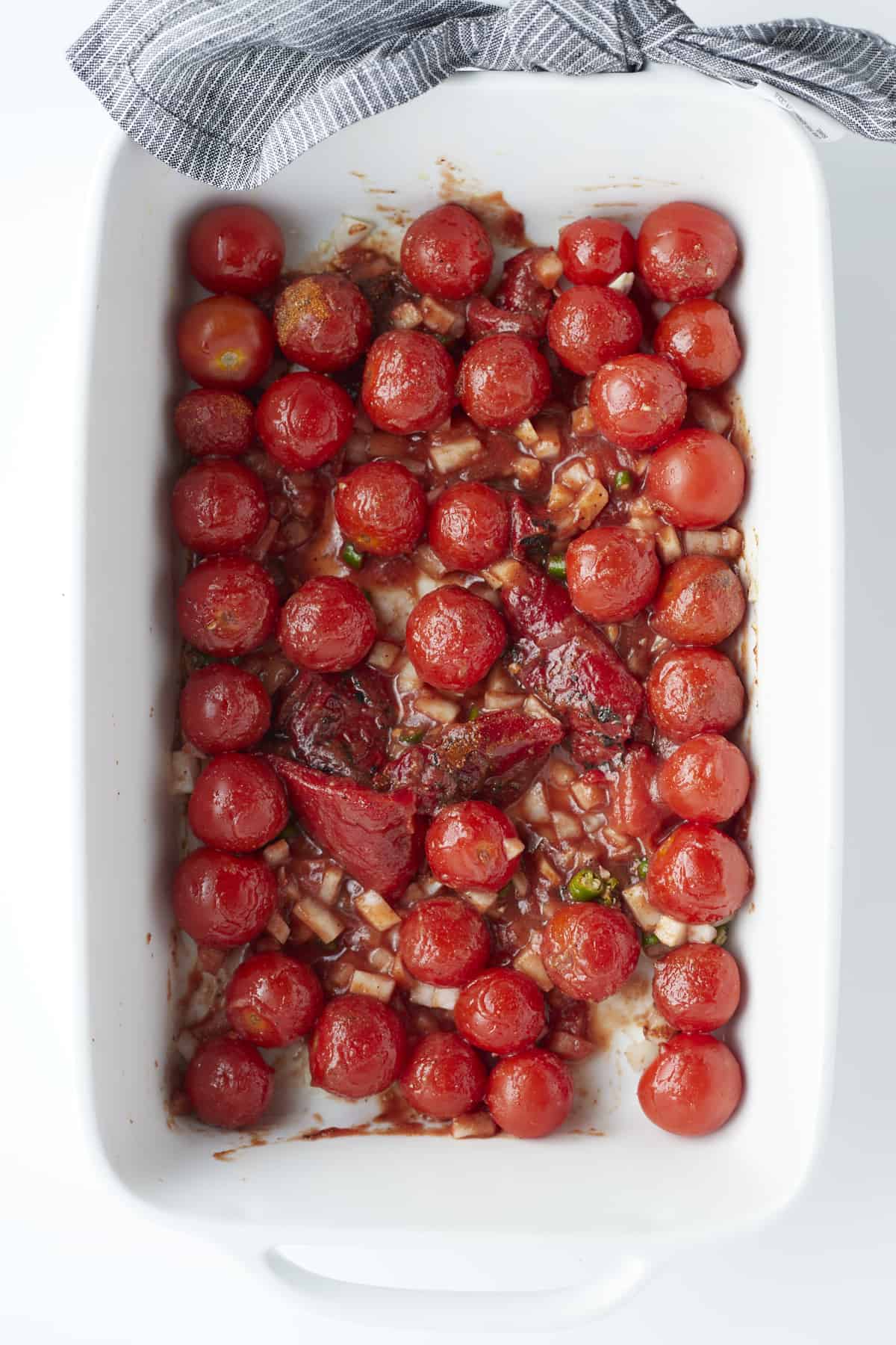 overhead image of a baking dish with cherry tomatoes and herbs