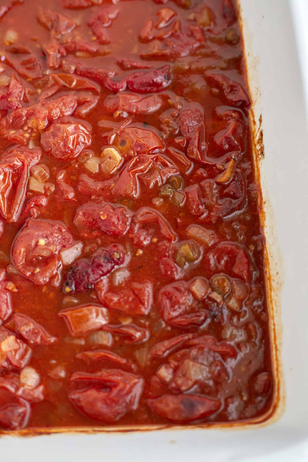 cherry tomatoes mashed with herbs in a baking dish to form the base of oven baked shakshuka