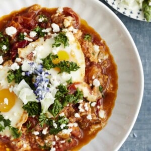 a bowl of oven baked shakshuka topped with feta, herbs, and edible flowers
