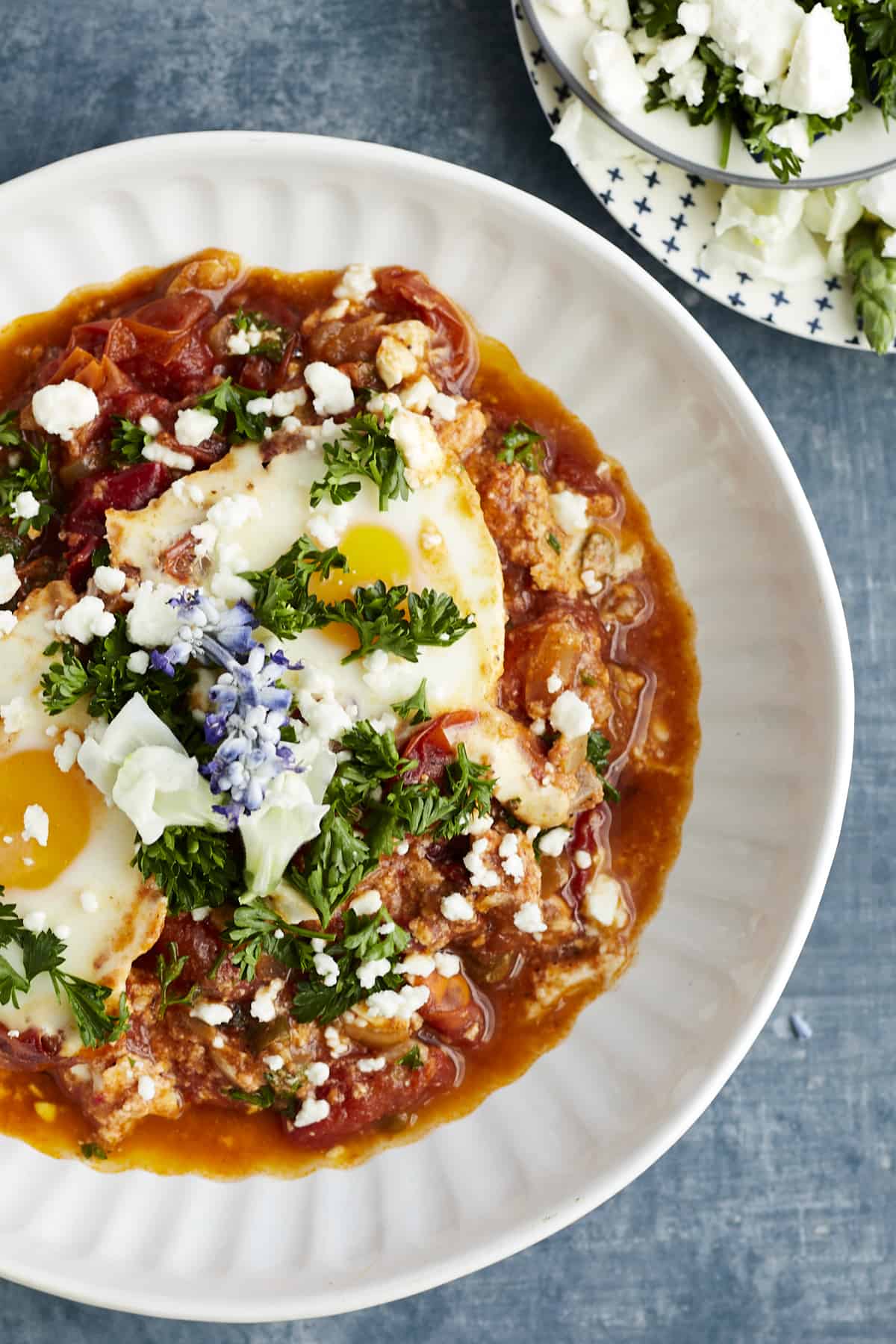 a plate of oven baked shakshuka topped with feta, fresh herbs, and edible flowers