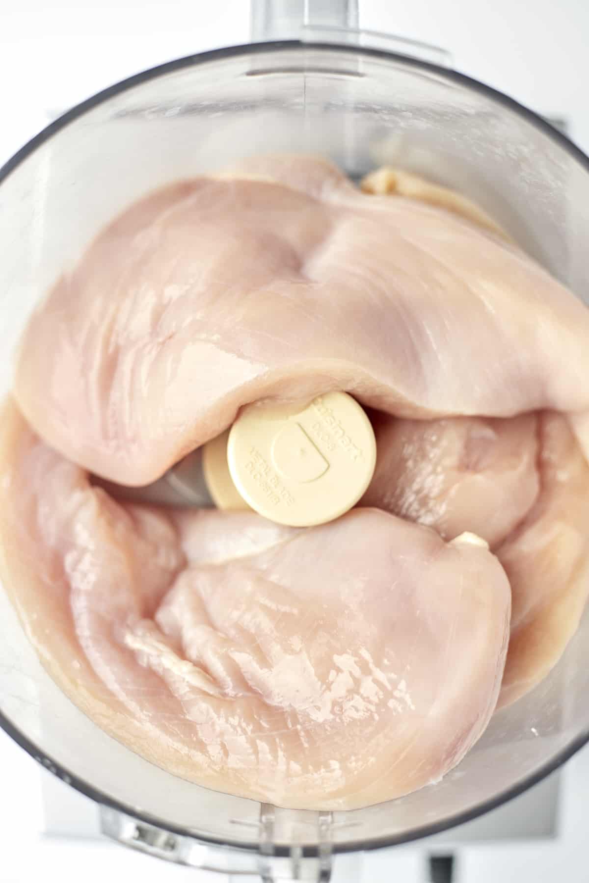 overhead image of chicken breasts in a food processor