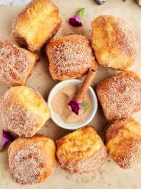 cinnamon bun air fryer french toast buns on a piece of parchment paper with a bowl of cinnamon sugar in the center