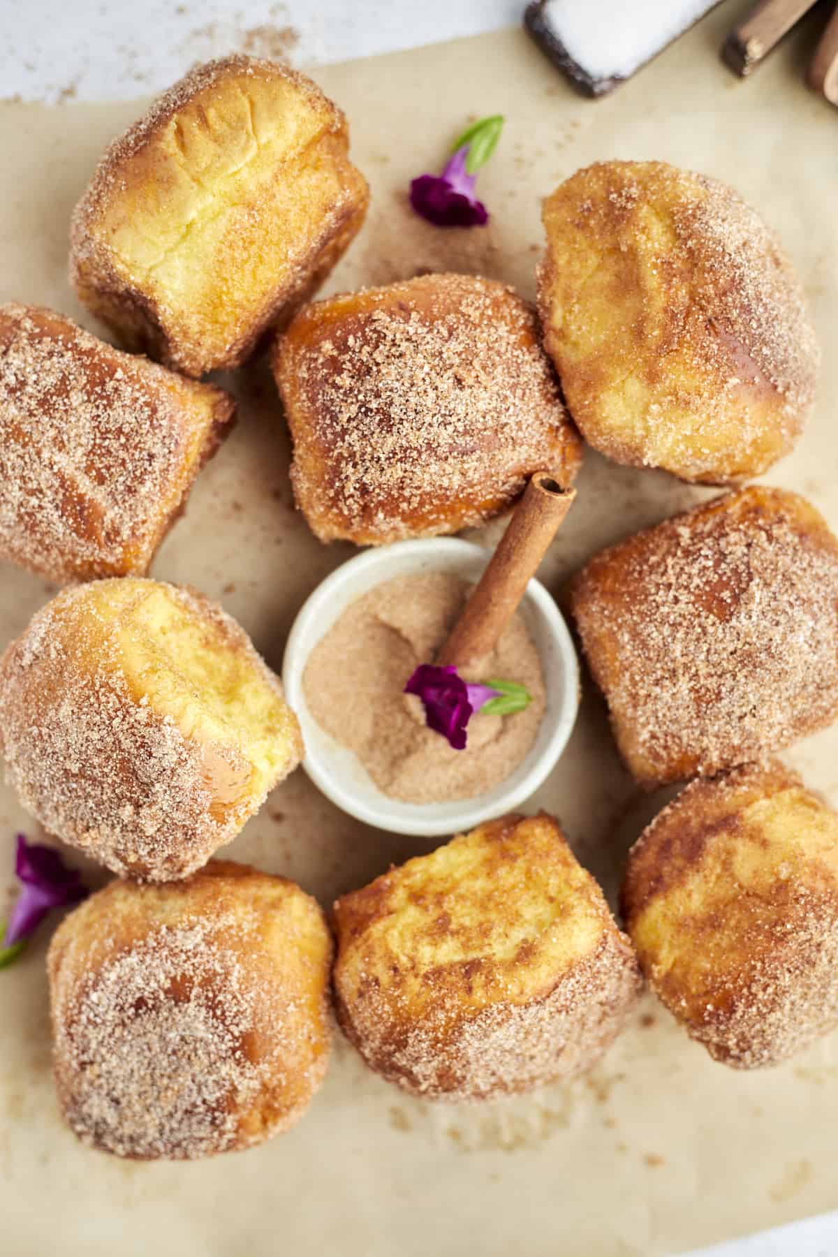 cinnamon french toast buns arranged on parchment paper with a bowl of cinnamon sugar 
