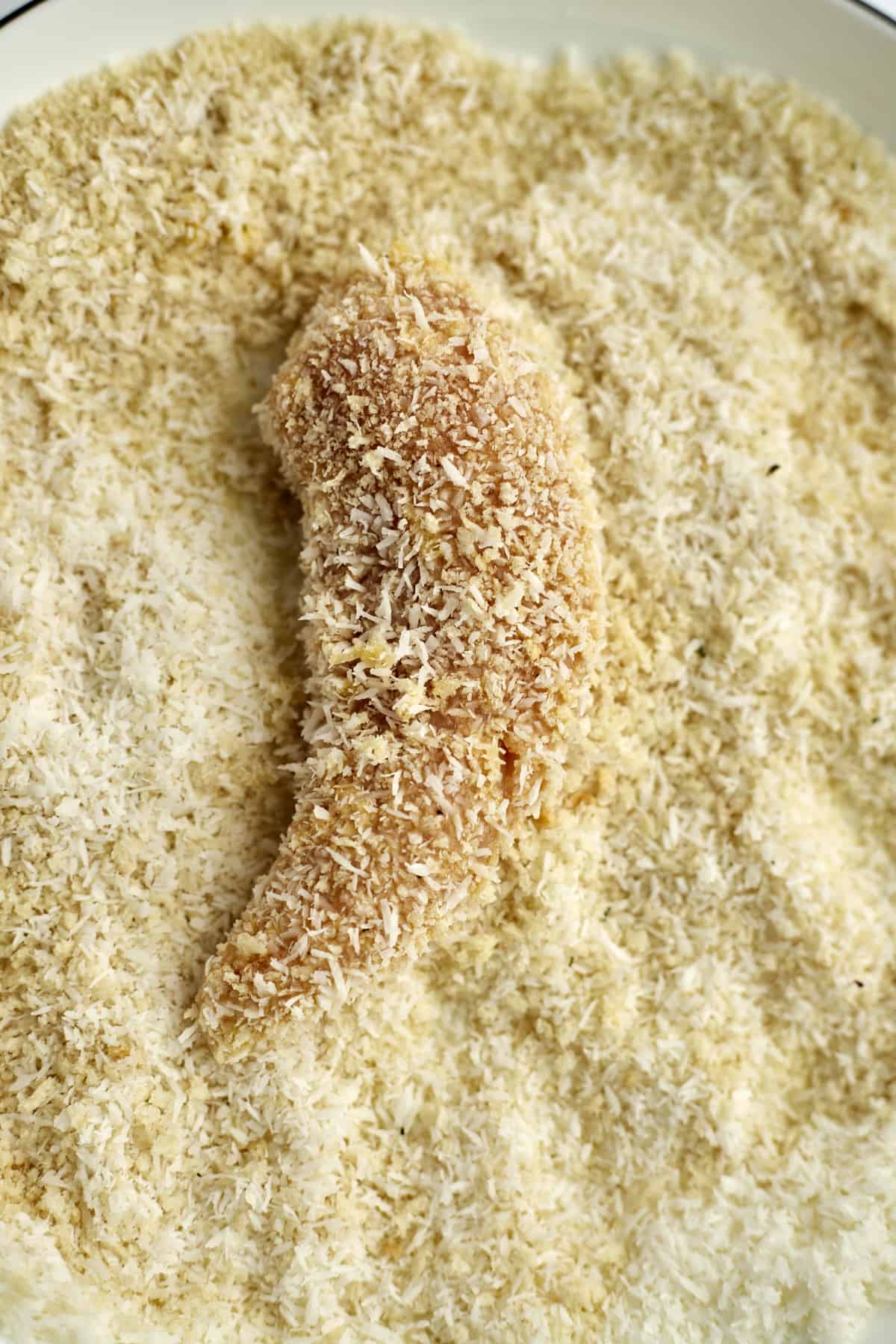 a raw chicken tender in a breadcrumb mixture