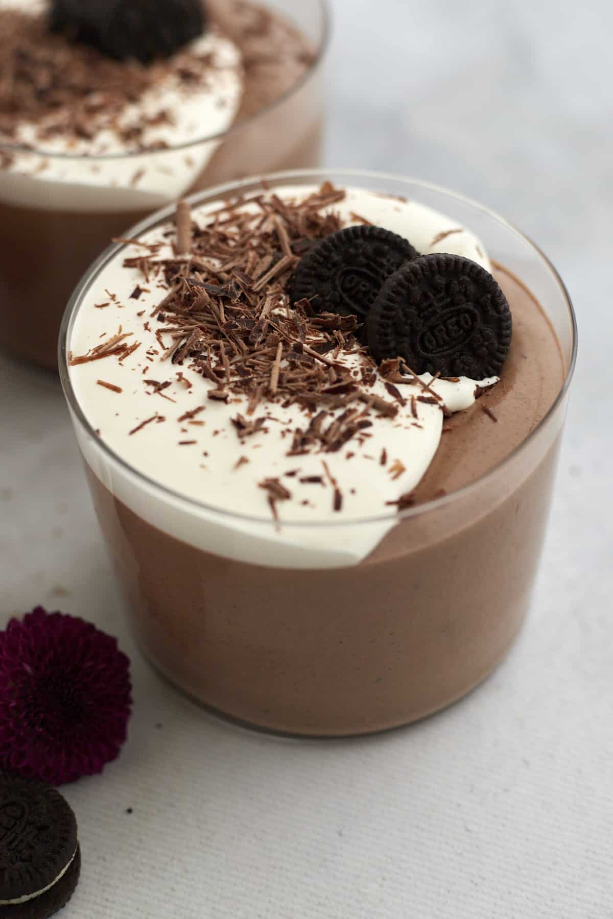 side view of oreo chocolate mousse in two ramekins garnished with whipped cream, chocolate, and oreo cookies.