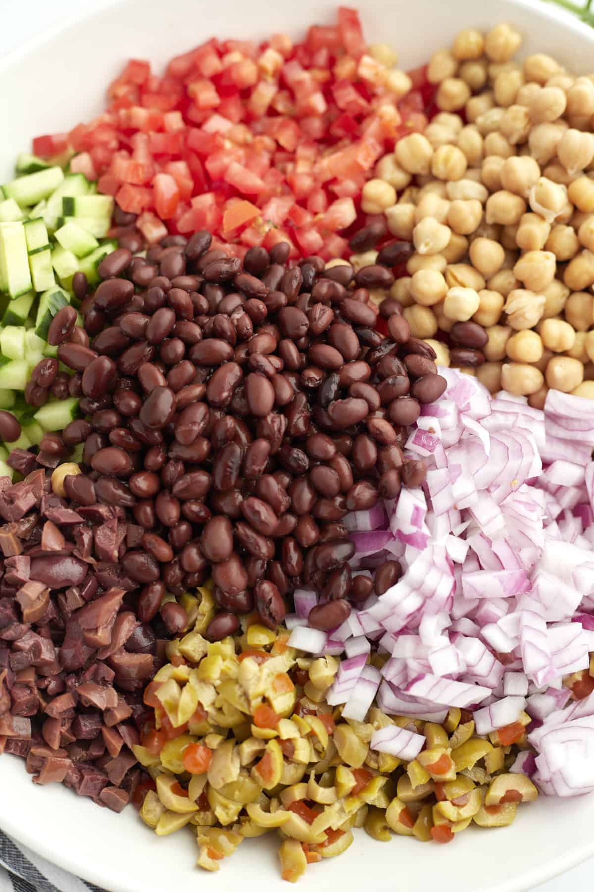 chopped tomatoes, chickpeas, red onion, corn, black beans, olives, and cucumbers in a bowl.