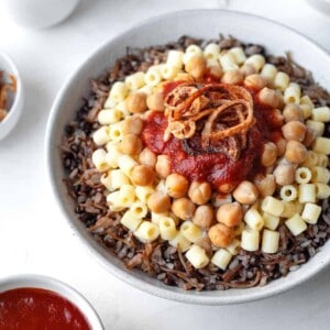 a bowl of Egyptian koshari with rice, pasta, chickpeas, tomato sauce, and crispy onions