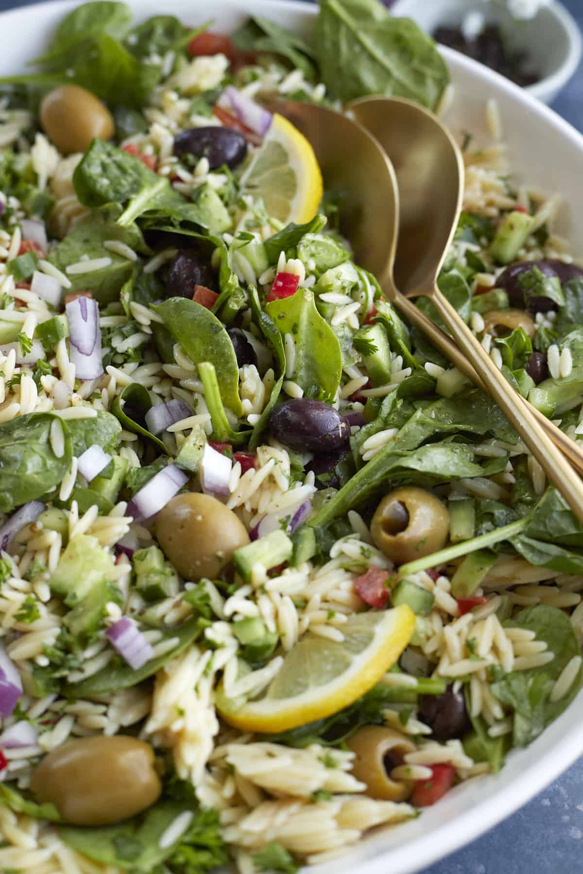 close up image of a bowl of Greek orzo pasta salad with serving spoons