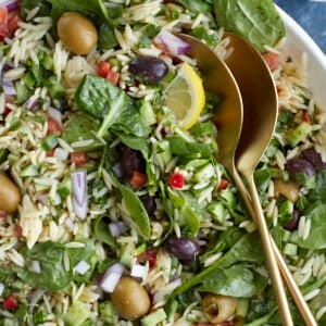 a bowl of Greek orzo pasta salad with two serving spoons on top