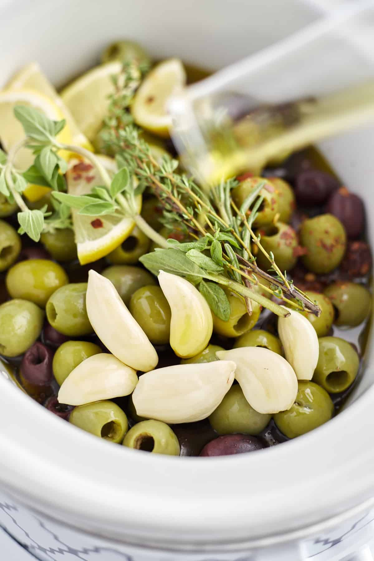 green and red olives, lemon wedges, garlic, and herbs in a slow cooker to make roasted olives