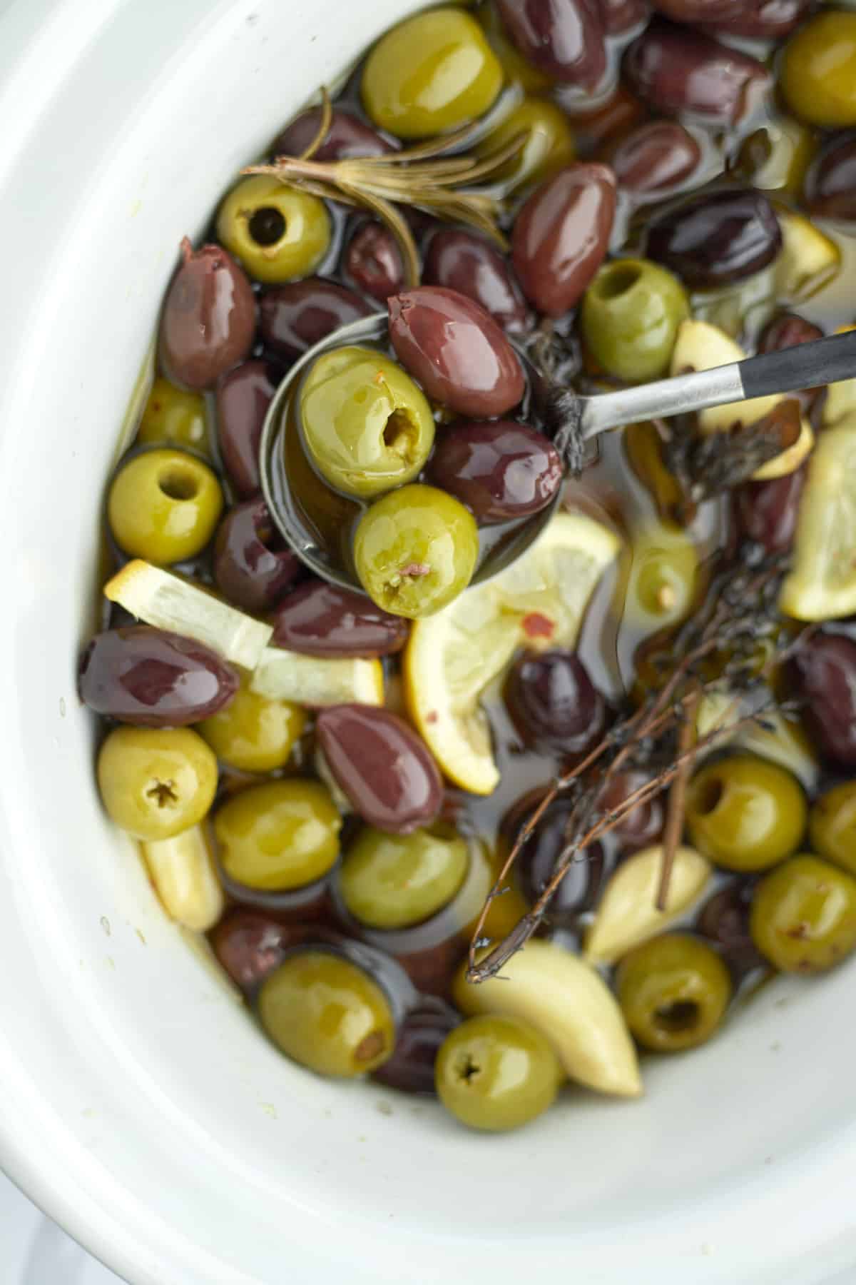 roasted olives being lifted out of a slow cooker with a spoon