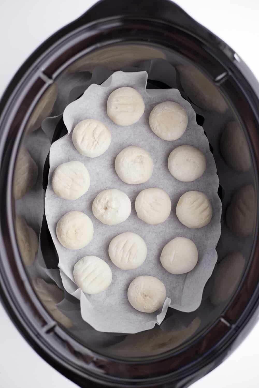 frozen dinner rolls arranged in the bottom of a parchment line slow cooker