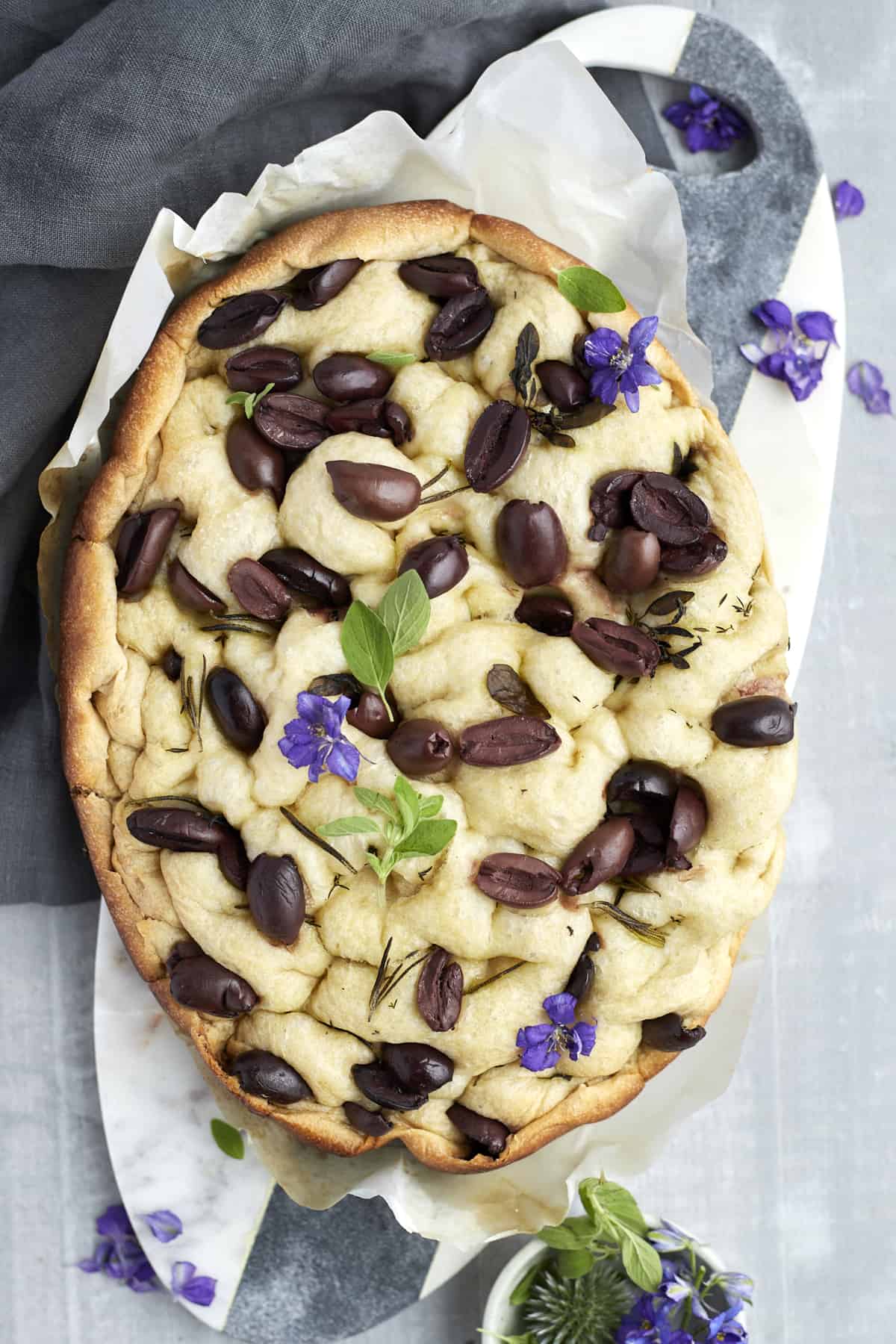 focaccia bread with kalamata olives on a marble slab garnished with fresh basil