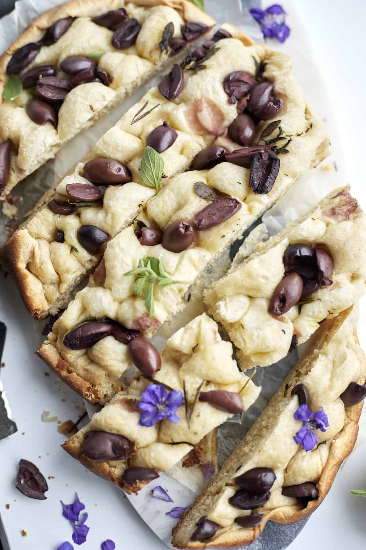 focaccia bread with kalamata olives on a marble slab garnished with fresh basil
