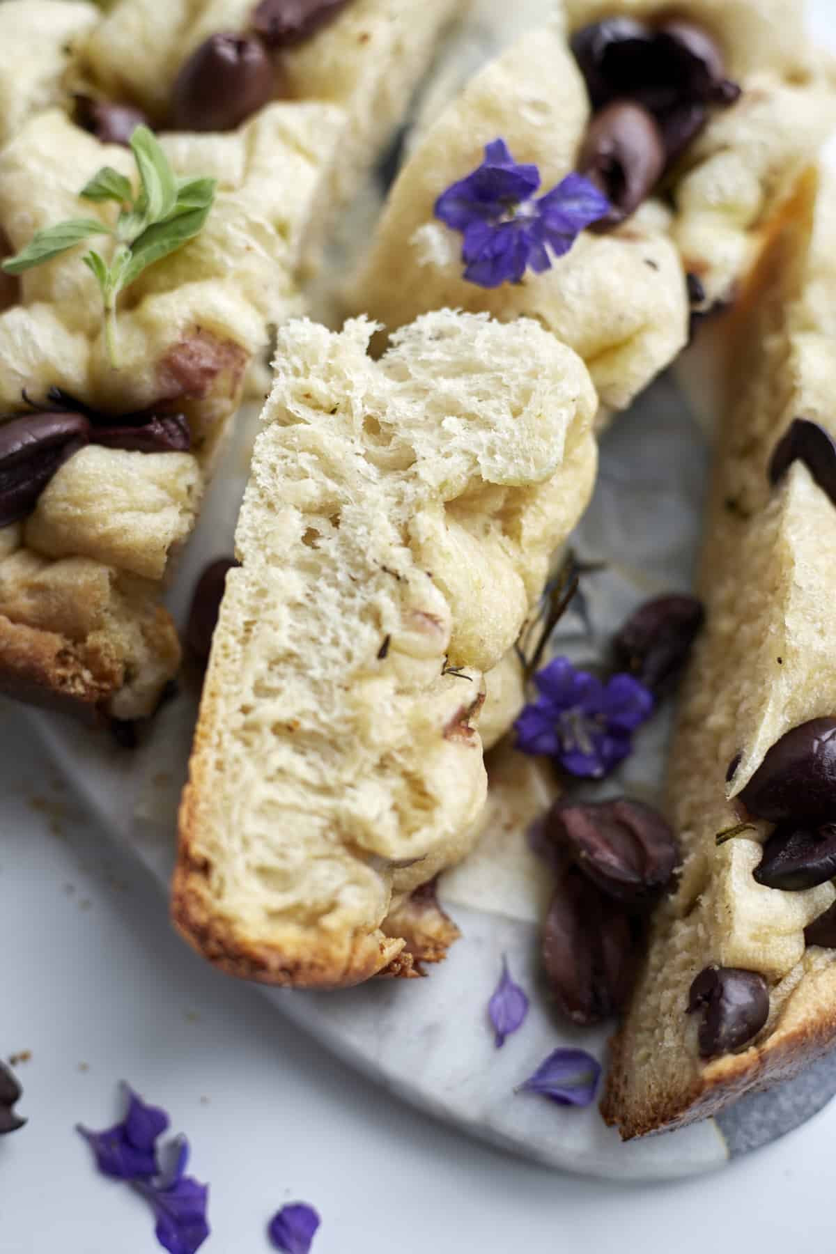 closeup focaccia bread with kalamata olives on a marble slab garnished with fresh basil