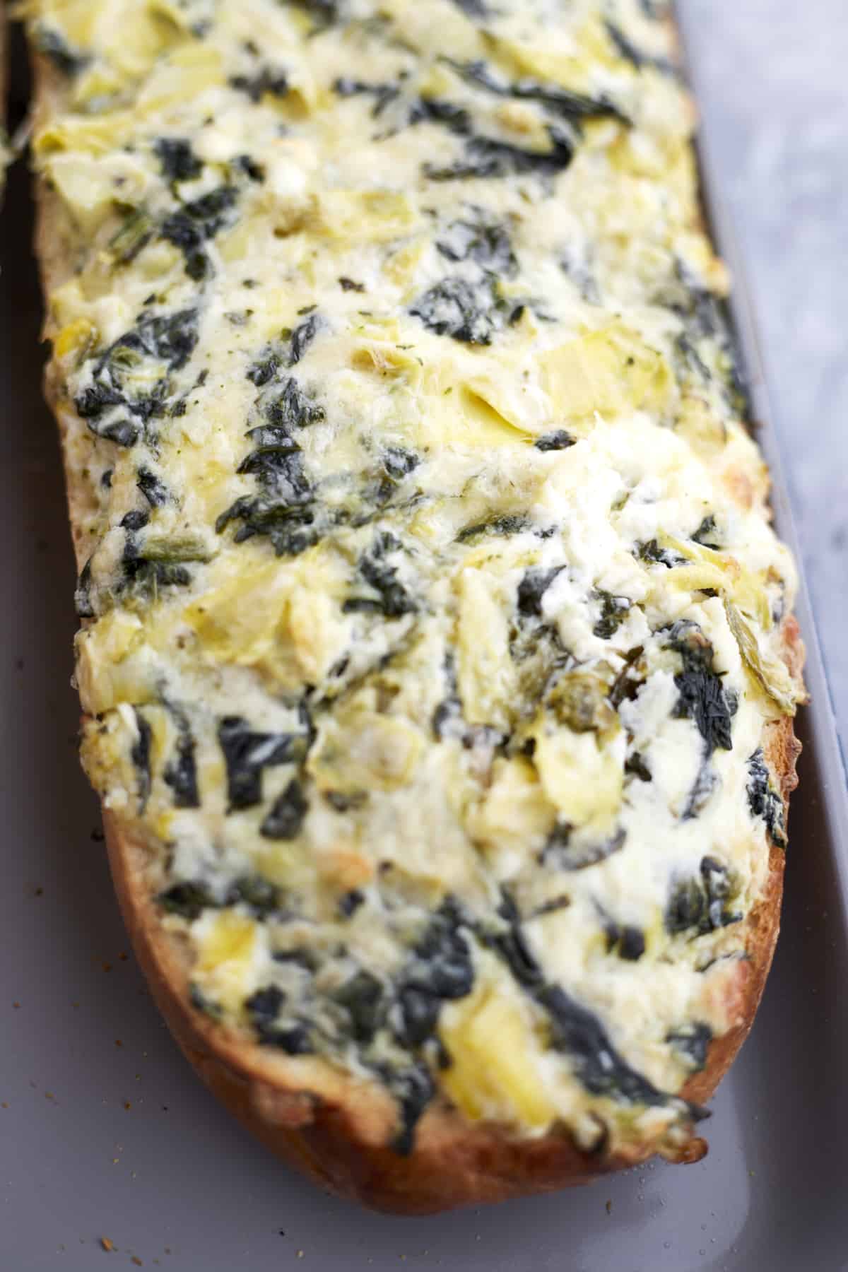 a cooked loaf of homemade garlic bread with spinach and artichoke dip topping