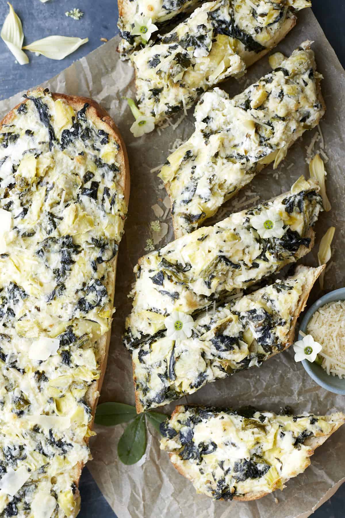 a whole loaf of homemade garlic bread with spinach and artichokes next to sliced pieces of garlic bread