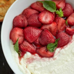 close up image of whipped goat cheese with strawberries in a white baking dish topped with mint