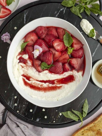 whipped goat cheese with baked strawberries in a white serving bowl topped iwth mint