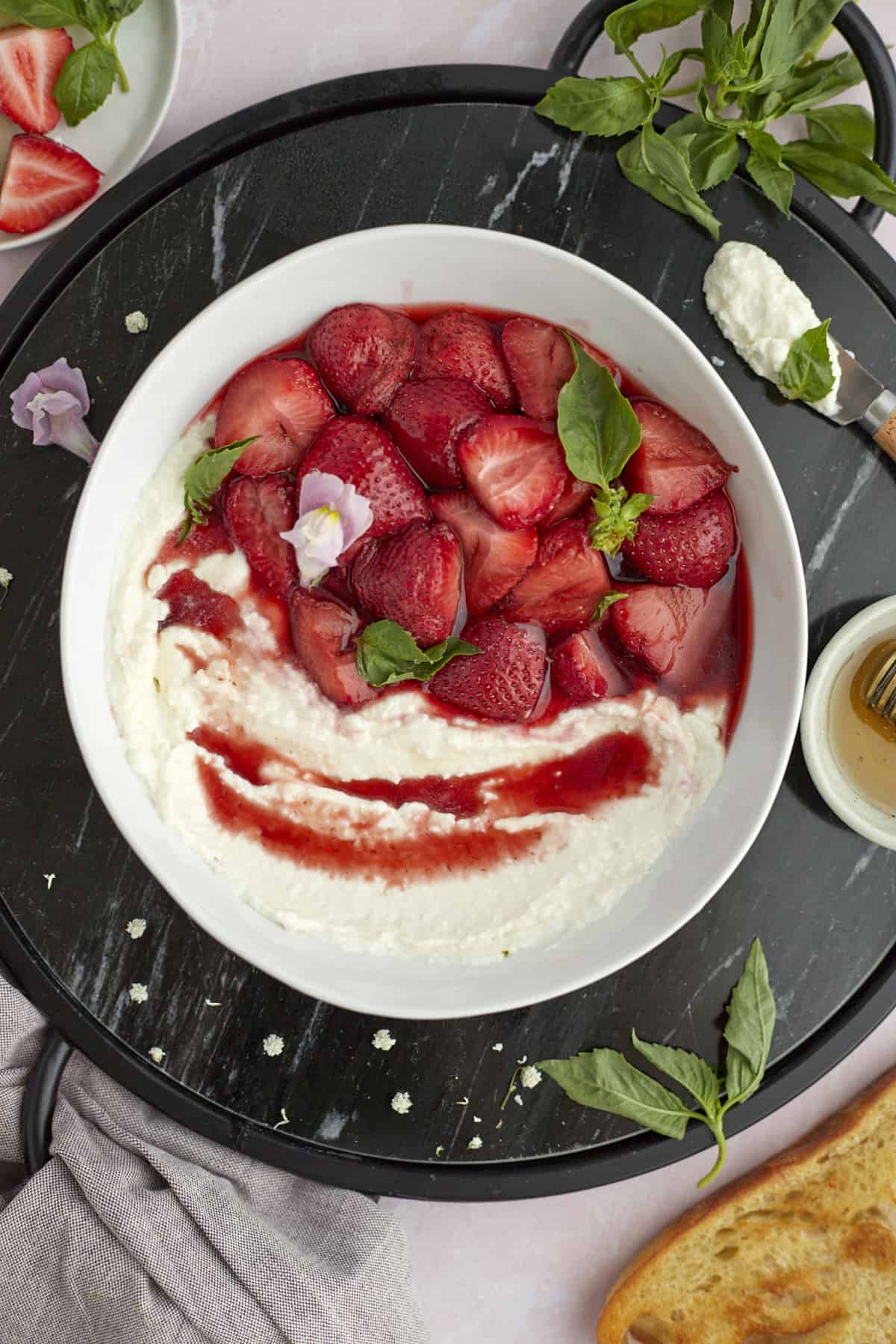 Bowl of whipped goat cheese topped with roasted strawberries and fresh basil